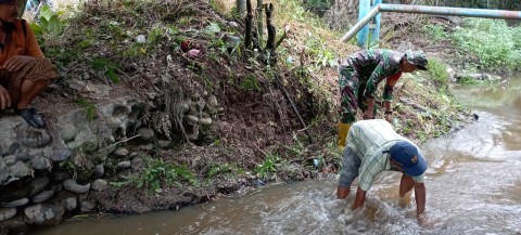 Sertu MB Simanjuntak bersama warga bersihkan aliran parit di wilayah binaan.